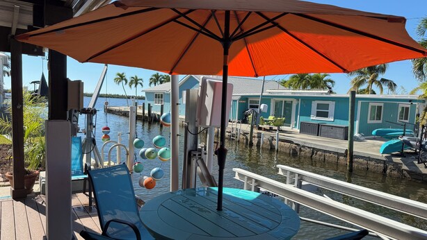 A covered outdoor seating area with a table and chairs, overlooking a marina with boats and a dock. - Orange You Glad Cottage - A Fisherman’s  Paradise in sunny Matlacha (Matlacha)