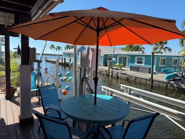 Un área de estar al aire libre techada con una mesa y sillas, con vista a una marina con barcos y un muelle.