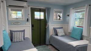 A bedroom with two beds, a green door, and a window with a bird. - Orange You Glad Cottage - A Fisherman’s  Paradise in sunny Matlacha (Matlacha)
