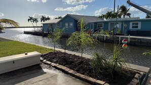 A waterfront property with a dock, a small boat, and a blue building with a sloped roof. - Orange You Glad Cottage - A Fisherman’s  Paradise in sunny Matlacha (Matlacha)