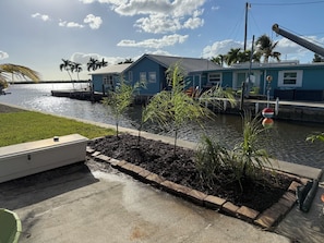 Una propiedad frente al agua con un muelle, un barco pequeño y un edificio azul con techo inclinado.