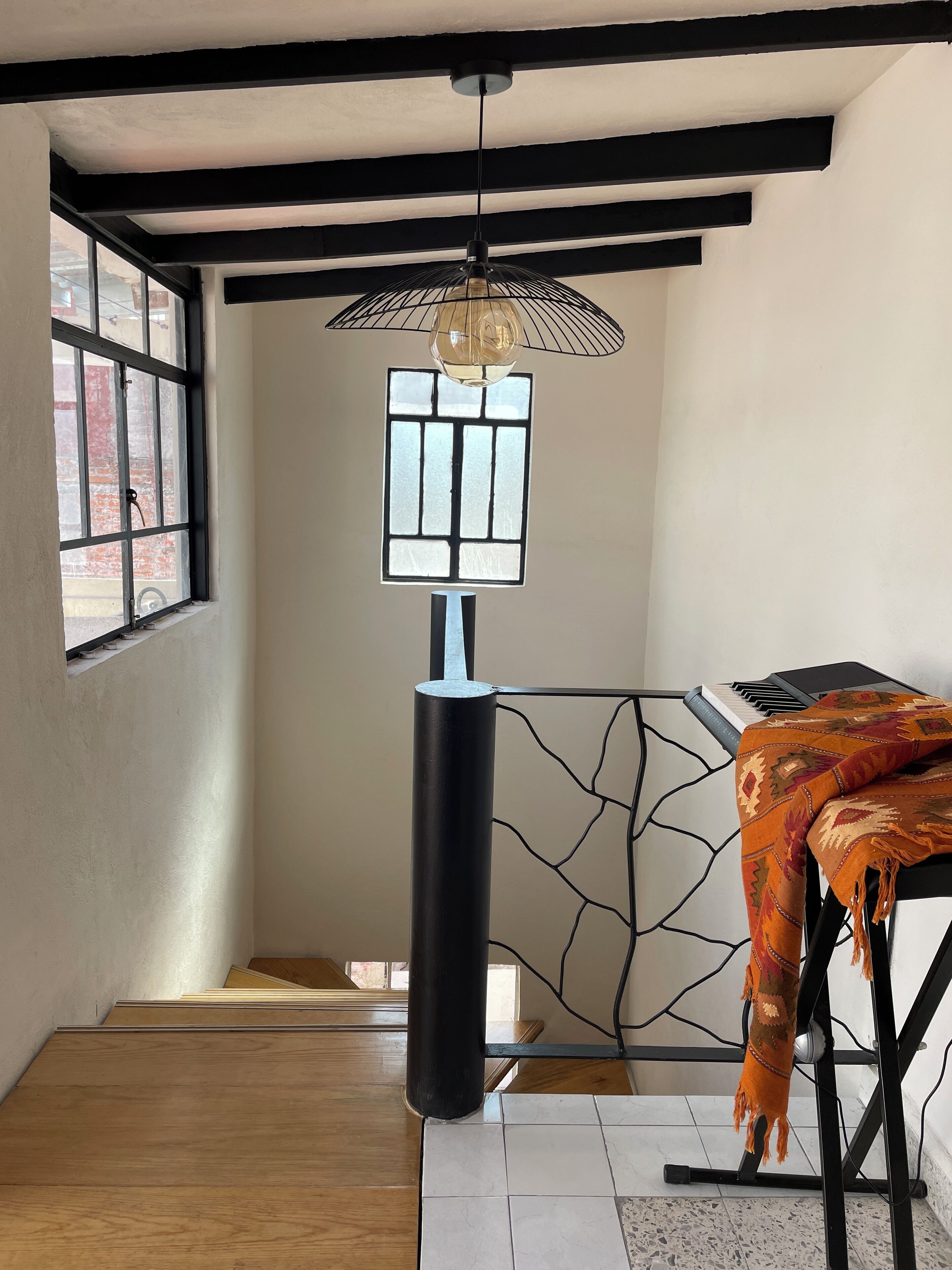 A room with a piano, a modern pendant light, and a patterned throw on the piano.