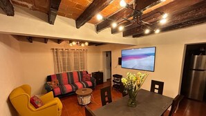 A living room with a sofa, yellow armchair, dining table, and a flat-screen TV mounted on the wall. - Casa Vecindad Murales - Secret Mural Home in Coyoacán (Ciudad de México)