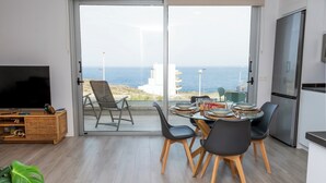 Een moderne woonkamer met een grote schuifpui naar een balkon met uitzicht op zee.