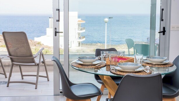 Een eetgedeelte met een glazen tafel, stoelen en uitzicht op de zee.