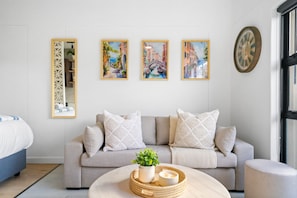 A modern living room with a sofa, decorative pillows, a coffee table with a plant and candles, and three framed paintings on the wall. - Studio on North (Cape Town)