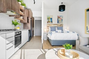 A modern kitchen with built-in appliances, a dining area with a round table, and a bedroom with a large bed and a nightstand. - Studio on North (Cape Town)