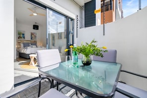 A glass-top table with a potted plant and two glasses, a white chair, and a view of a bedroom with a bed and a ceiling fan. - Studio on North (Cape Town)
