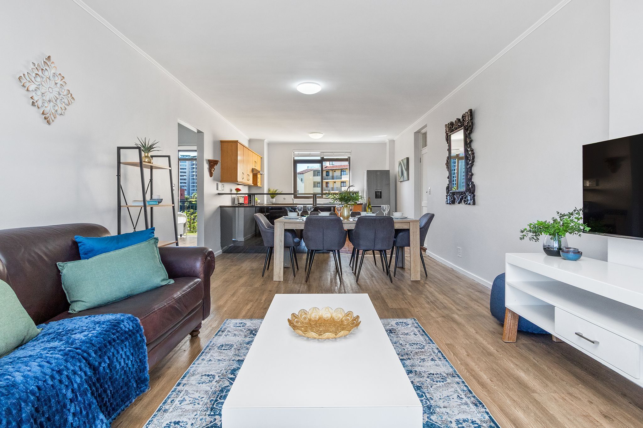 A modern living room with a brown leather sofa, a white coffee table, and a dining area with a wooden table and chairs.