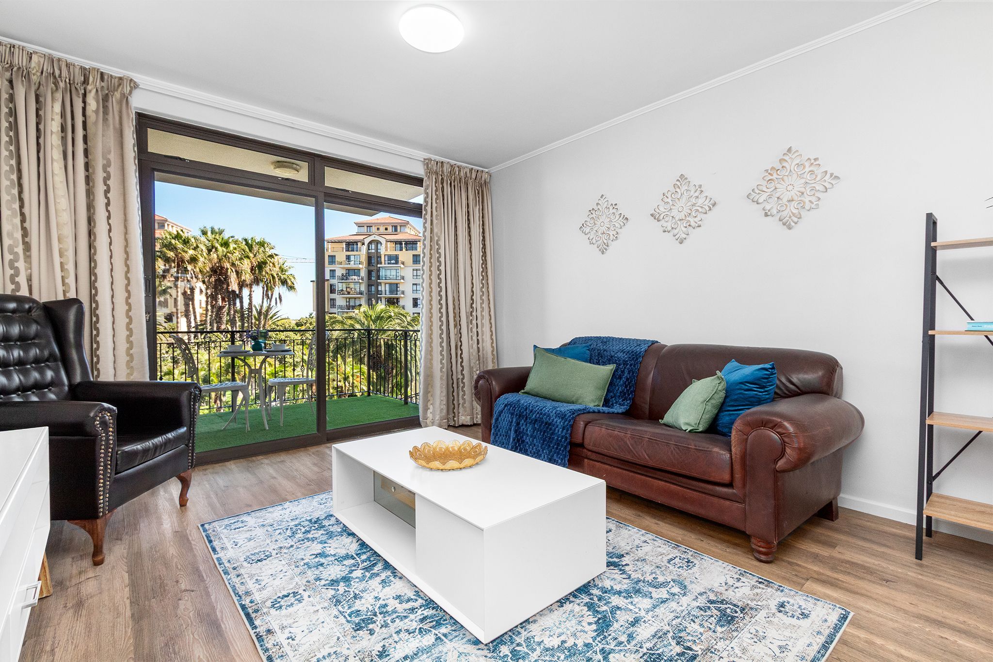 A living room with a brown leather sofa, a white coffee table, and a black leather armchair.