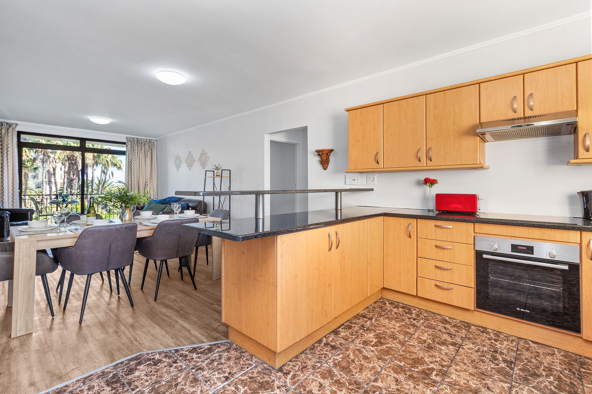 A modern kitchen with wooden cabinets, a Bosch oven, and a dining area with a marble countertop.