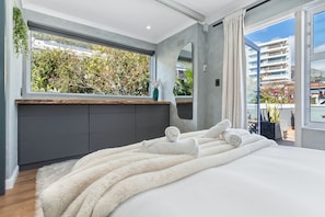 A modern bedroom with a large bed, a view of greenery outside, and a balcony with plants. - Selbourne Five (Cape Town)
