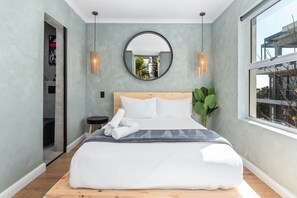 A modern bedroom with a large bed, a round mirror, and a view of the outdoors. - Selbourne Five (Cape Town)