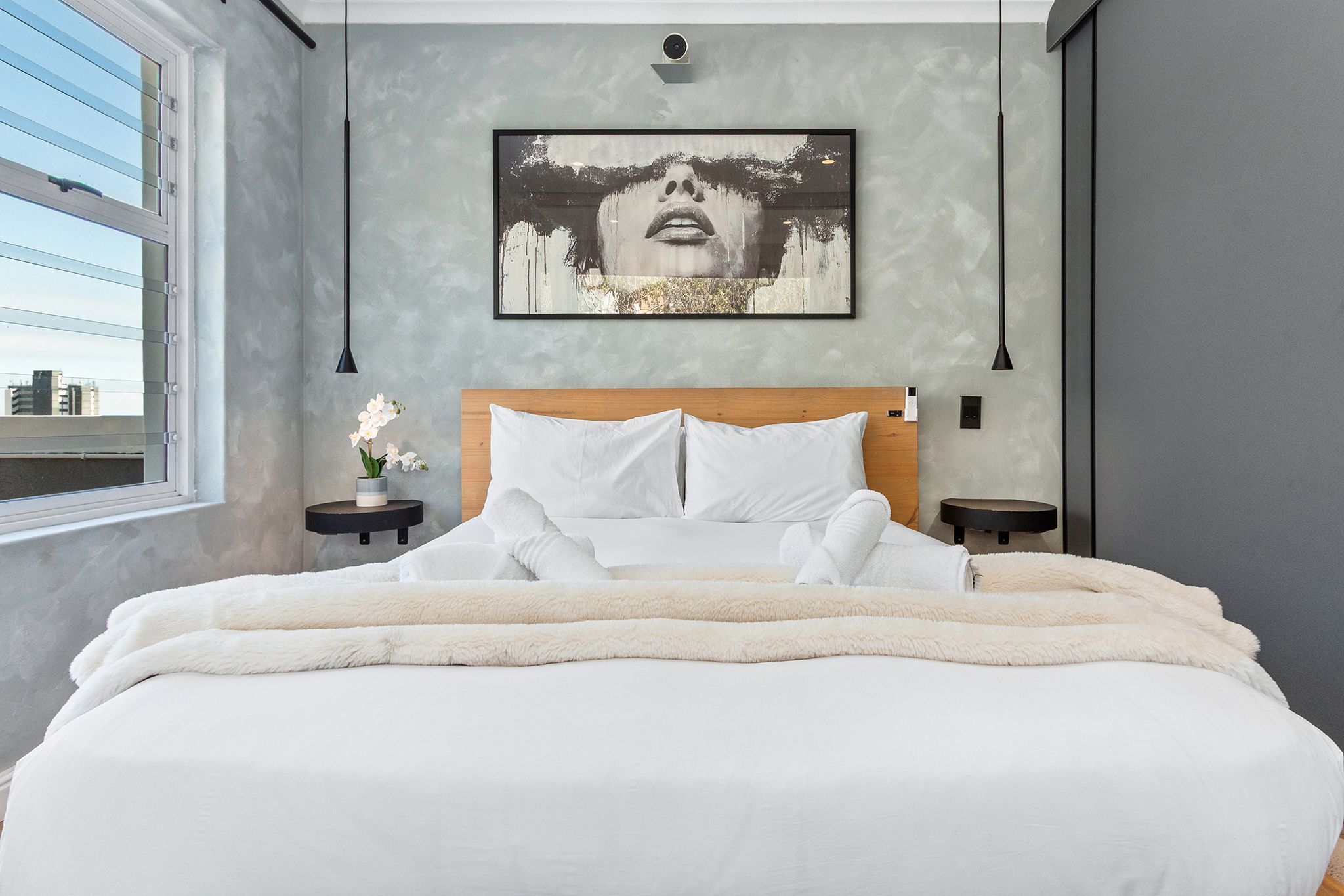 A modern bedroom with a large bed, a city view, and a framed artwork on the wall.