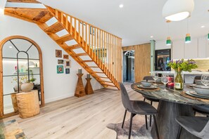 Ein modernes Interieur mit einer Holztreppe, einem Essbereich mit rundem Tisch und einer Küche im Hintergrund.