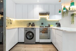A compact kitchen with white cabinetry, a built-in washing machine, a microwave, and a coffee maker. - Selbourne Five (Cape Town)