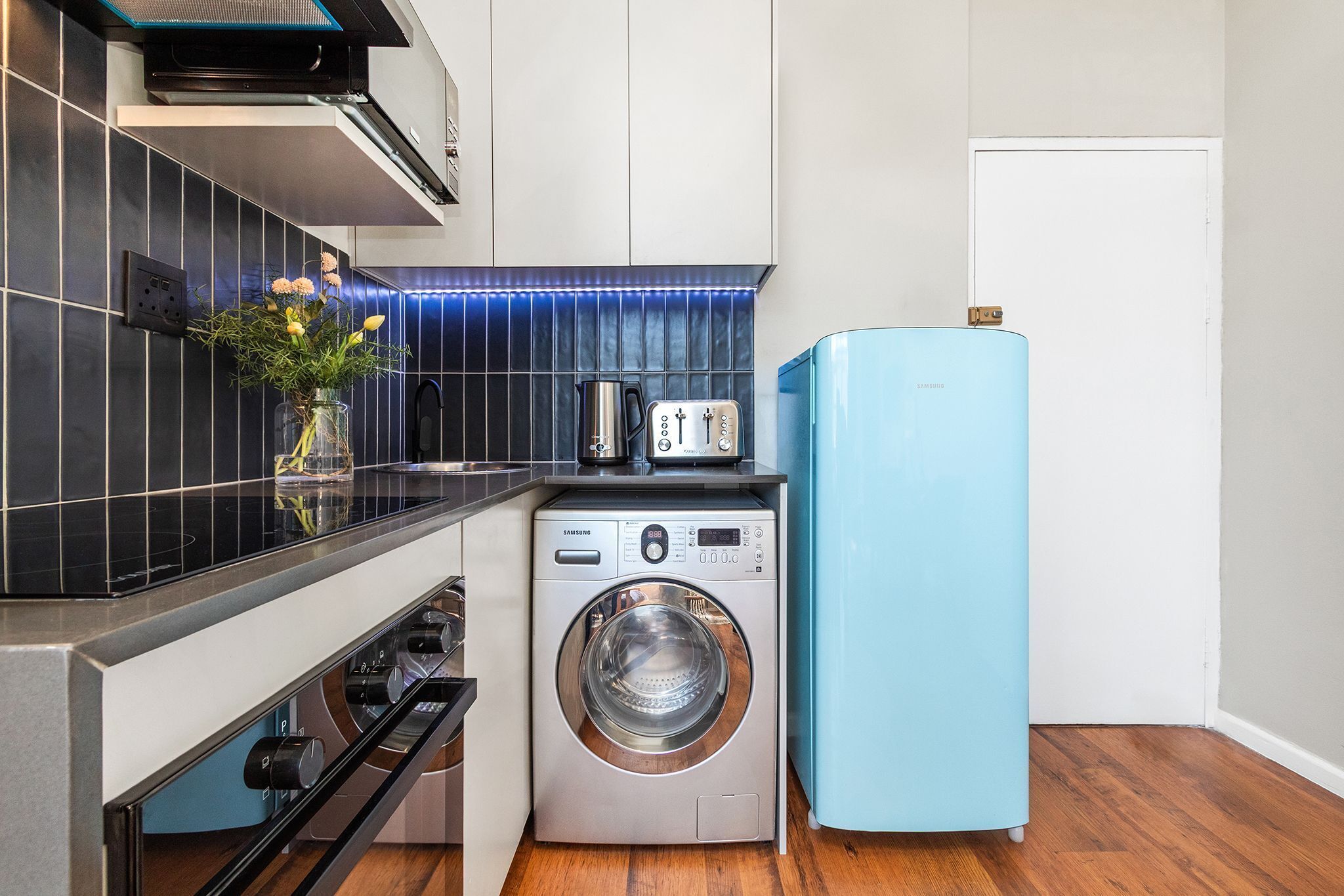 Une cuisine compacte équipée d’un lave-linge, d’un grille-pain et d’un réfrigérateur bleu.