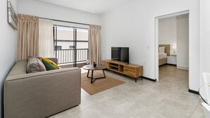 Ein modernes Wohnzimmer mit einer Couch, einem Fernseher auf einem Holzboden und einem großen Fenster mit Vorhängen.