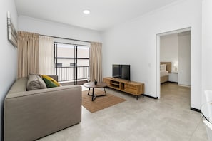 A modern living room with a sofa, a TV on a wooden stand, and a large window with curtains. - Mandalay Hideaway (Johannesburg)