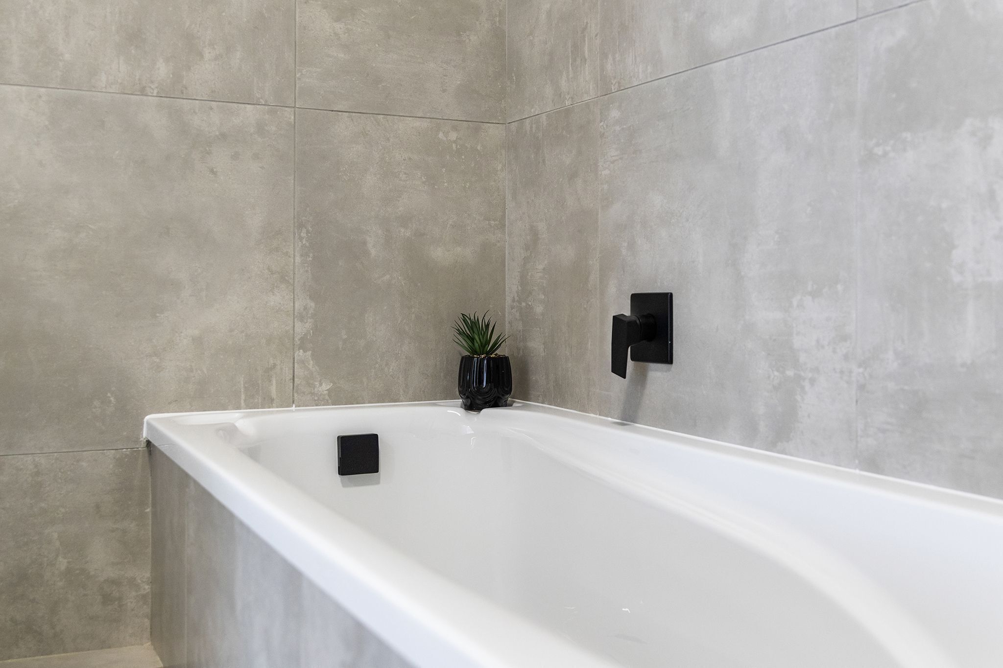 Een moderne badkamer met een groot wit bad, een kleine potplant en een zwarte handdoekhouder.