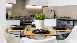 A modern kitchen with a glass dining table, white chairs, a potted plant, and a built-in oven. - Mandalay Hideaway (Johannesburg)