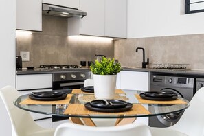 Eine moderne Küche mit einem Glastisch, weißen Stühlen, einem Blumentopf und einem eingebauten Backofen.