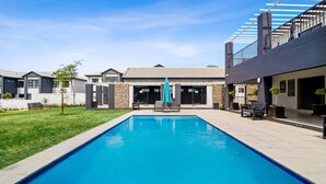 A rectangular swimming pool with a blue cover, surrounded by a patio area with outdoor seating and a stone wall. - Mandalay Hideaway (Johannesburg)