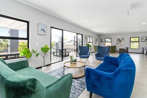 Ein geräumiger Raum mit großem Fenster, einem grünen Sofa, einem blauen Sofa und einem runden Couchtisch mit Pflanzen.