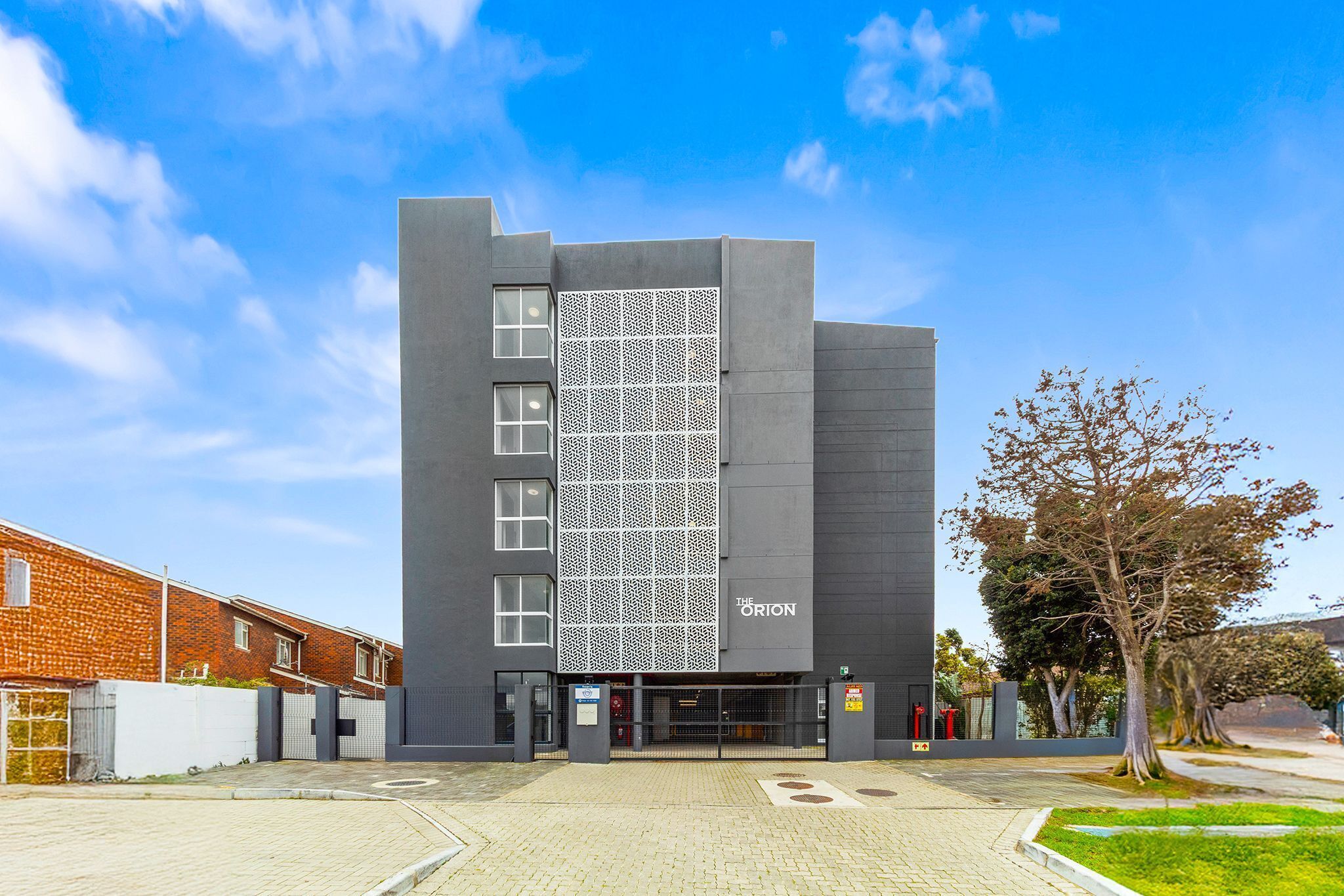 A modern building with a name sign, a patterned facade, and a gated entrance.