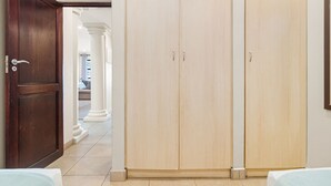 A hotel room with a wooden door, a large wardrobe, and a glimpse of a living area with a sofa and a window. - Bali Hai 103 (Westbrook)