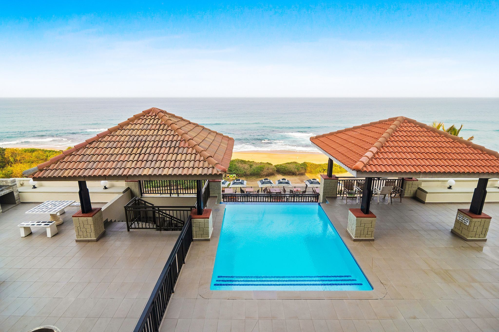 Piscina no terraço com duas tendas, espreguiçadeiras e vista para o mar.