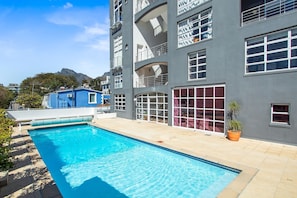 A modern building with a swimming pool, large windows, and a mountain in the background.