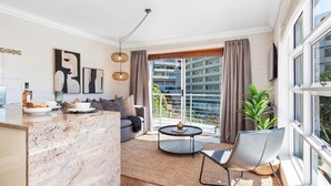 A modern living room with a sofa, a coffee table, and a dining area with a marble countertop. - Harbour Terrace 7 (Cape Town)