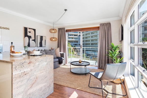 A modern living room with a sofa, a round coffee table, and a dining area with a marble countertop.