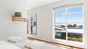 A modern hotel room with a large window offering a city view, a neatly made bed with white towels, and a wooden shelf with decorative items. - Harbour Terrace 7 (Cape Town)