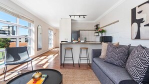 A modern living room with a grey sofa, black and white patterned pillows, a black coffee table, and a large window providing a view of the city. - Harbour Terrace 7 (Cape Town)