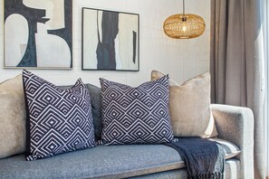 A modern living room with a grey sofa, patterned throw pillows, abstract wall art, and a woven pendant light.