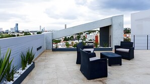 A rooftop terrace with modern outdoor furniture, a view of the cityscape, and a concrete structure.