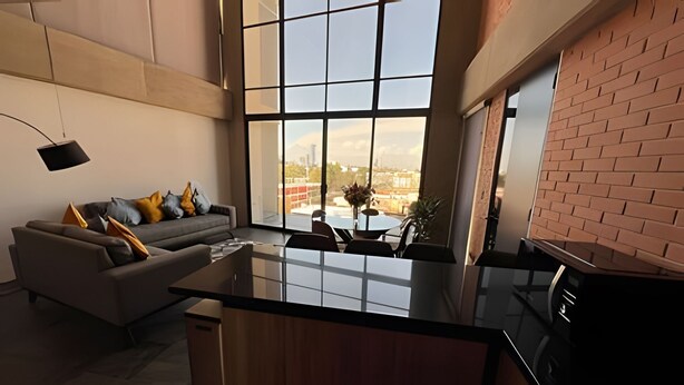 A modern kitchen with a large island, a dining area with a table and chairs, and a sofa with cushions.