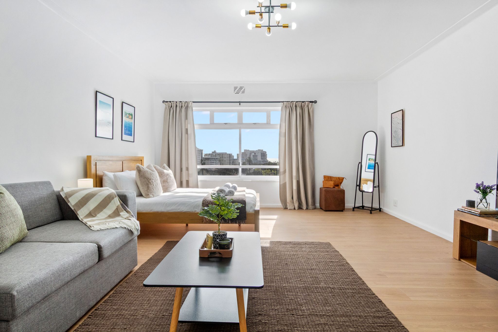 A modern living room with a sofa, a bed, a coffee table, and a view of the city through large windows.