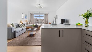 A modern living room with a grey sofa, a coffee table, and a view of the city through large windows. - E1 Ventnor House (Cape Town)