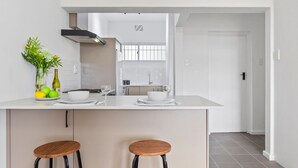 A modern kitchen with a central island, bar stools, and a view into the adjacent dining area. - E1 Ventnor House (Cape Town)