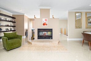 Un salon moderne avec une cheminée, un canapé vert, un sol en marbre et des objets décoratifs disposés sur des étagères.