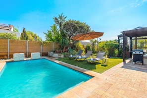Un jardin avec une piscine, des chaises longues, un barbecue et une pergola.