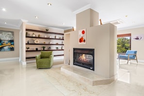 A spacious living room with a fireplace, a green armchair, and a bookshelf.