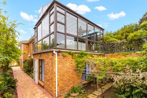 A modern house with a large glass conservatory, brick walls, and a garden with various plants. - Warwick Coastal Harmony (Cape Town)