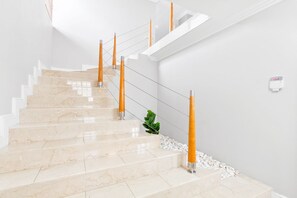 Un escalier avec des marches en marbre et des rampes en bois, menant à un palier avec un mur blanc et une petite plante.