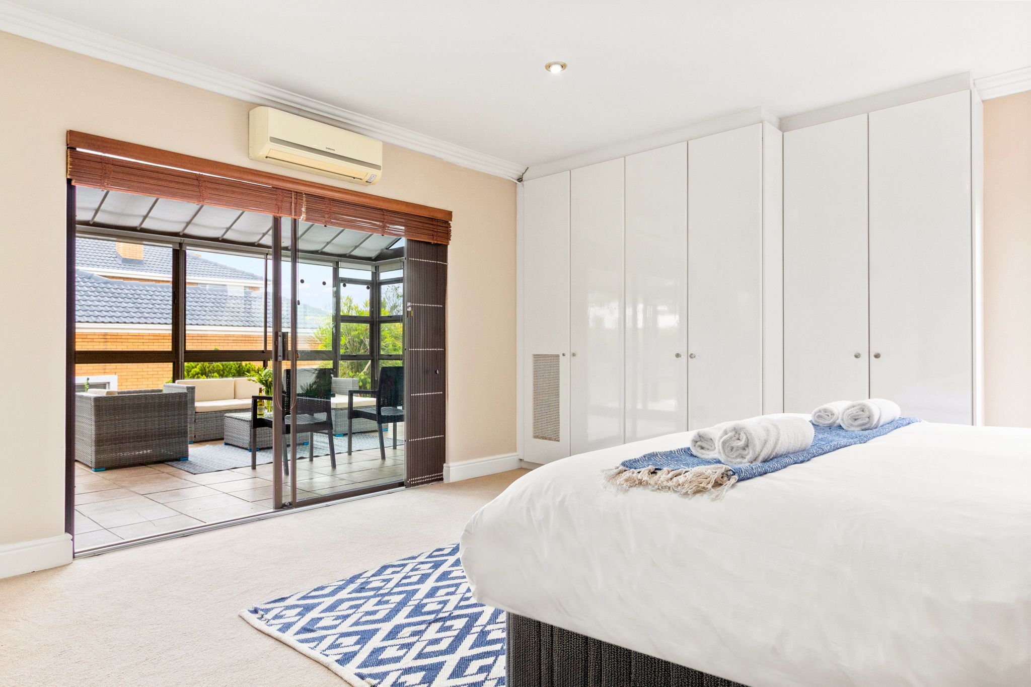 Une chambre d’hôtel comprenant un lit, une porte vitrée donnant sur un espace extérieur aménagé en coin salon, et une armoire.