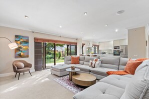 A modern living room with a sectional sofa, a round coffee table, and a dining area with a kitchen in the background. - Warwick Coastal Harmony (Cape Town)