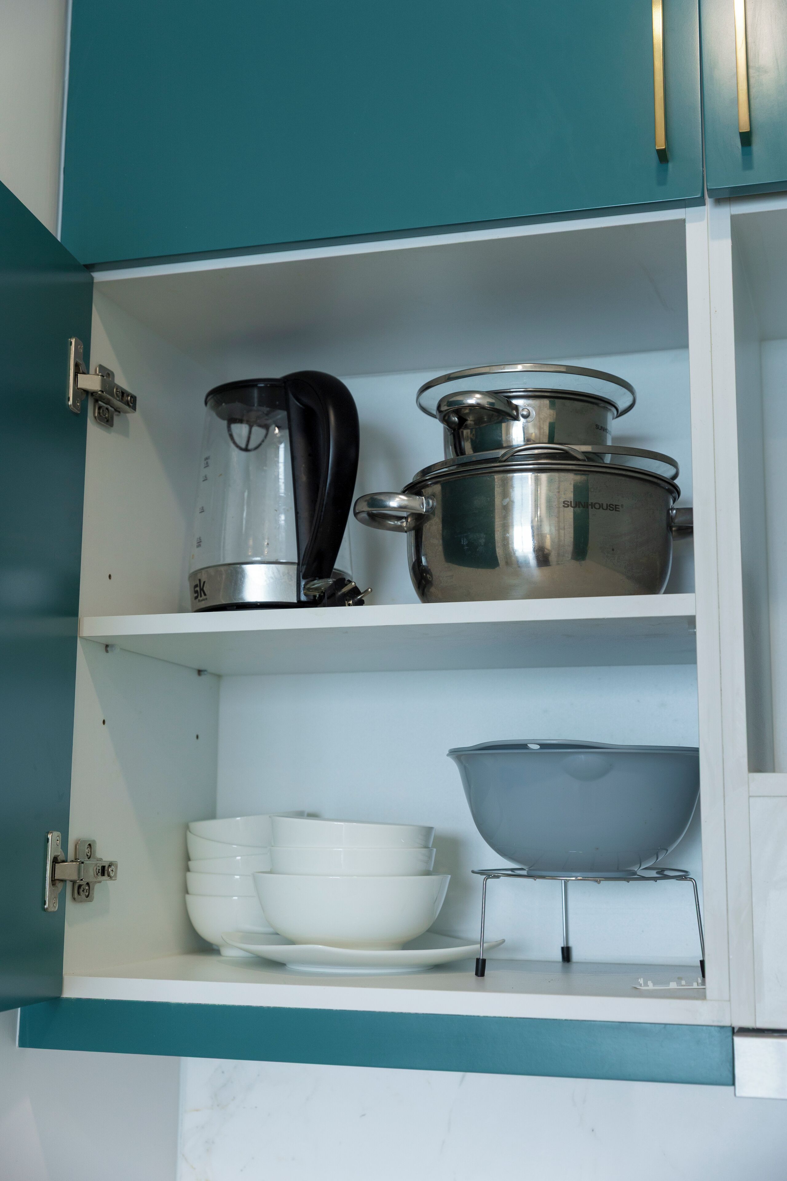A kitchen cabinet with stainless steel cookware, including a kettle, pots, and a griddle.